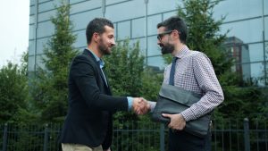Two businessmen shaking hands outside modern building — Abogado Chicago workers comp lawyer near me